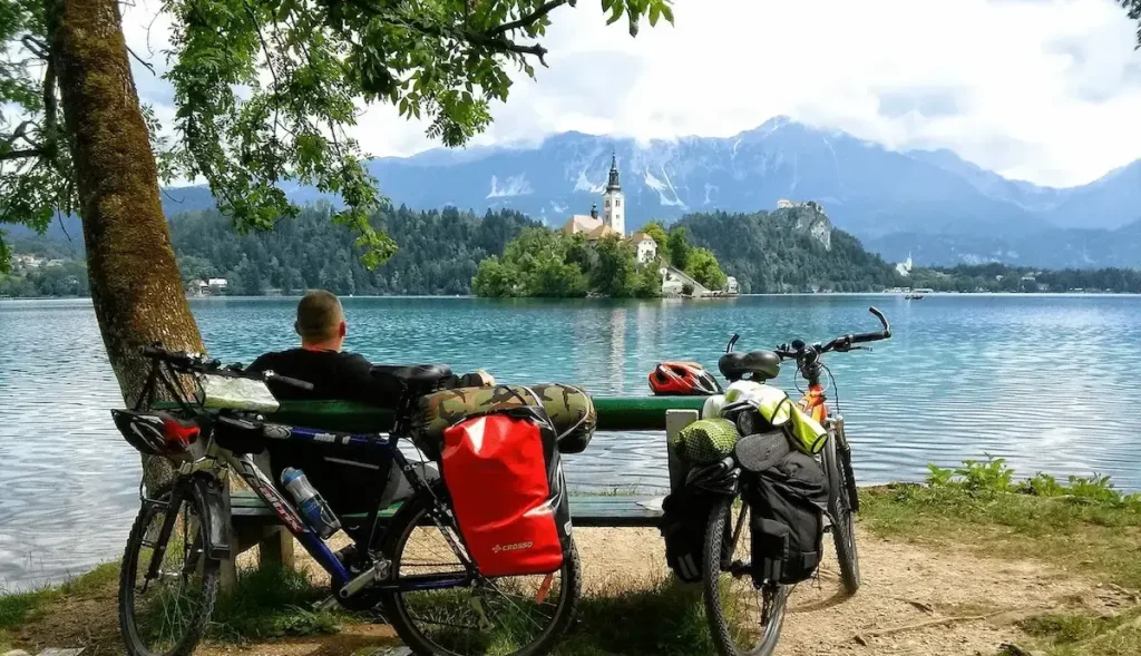 nagycsomagos bringás pihen a Bledi tó partján, és nézi a szigetet, templomot és az Alpokot a háttérben